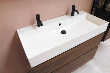 Drop-in white sink, dark wood vanity, black matte faucets, central drain, and a sleek modern design against a muted wall.